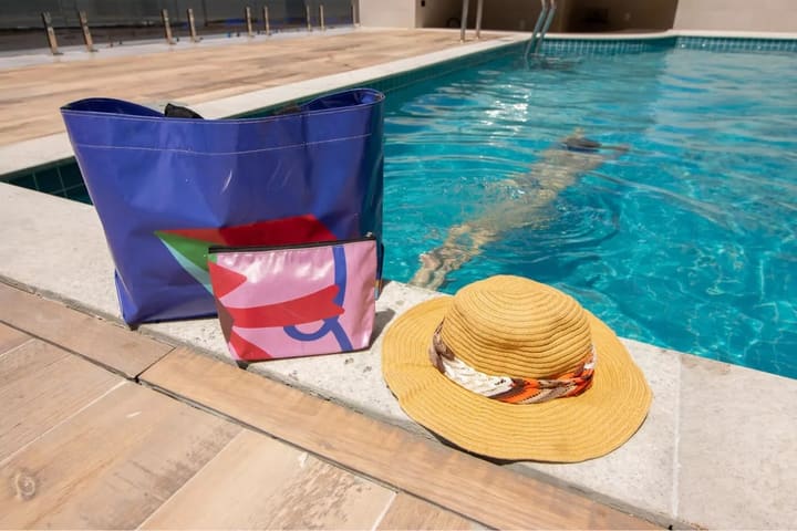 Bolsas e chapéu feitos de lona reaproveitada à beira de uma piscina.