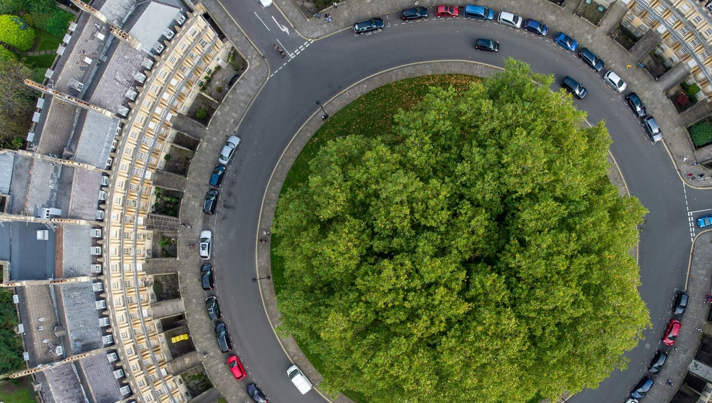 Vista aérea do Circus, em Bath, na Inglaterra: uma praça redonda coberta pela copa de grandes árvores, cercada por uma rua circular e por um anel contínuo de casas de pedra